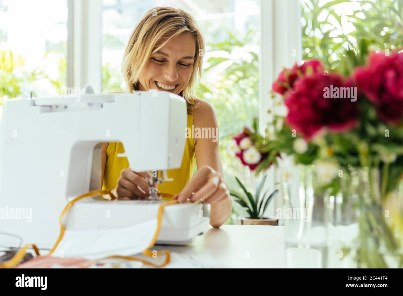 Lächelnde Frau näht Gesichtsmasken zu Hause Stockfoto