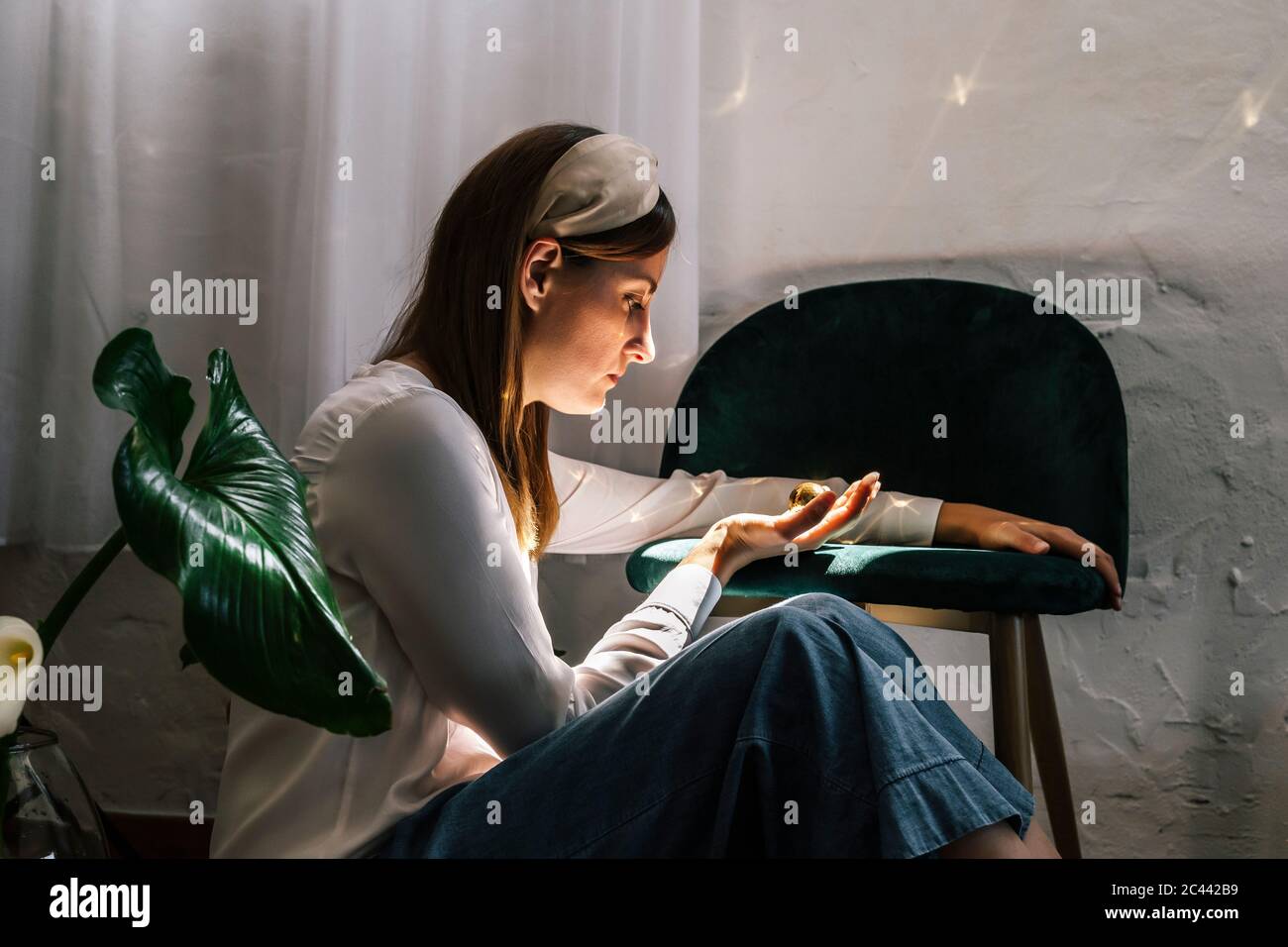 Frau, die auf goldene Kugel, während sie am Stuhl im Schlafzimmer sitzen Stockfoto
