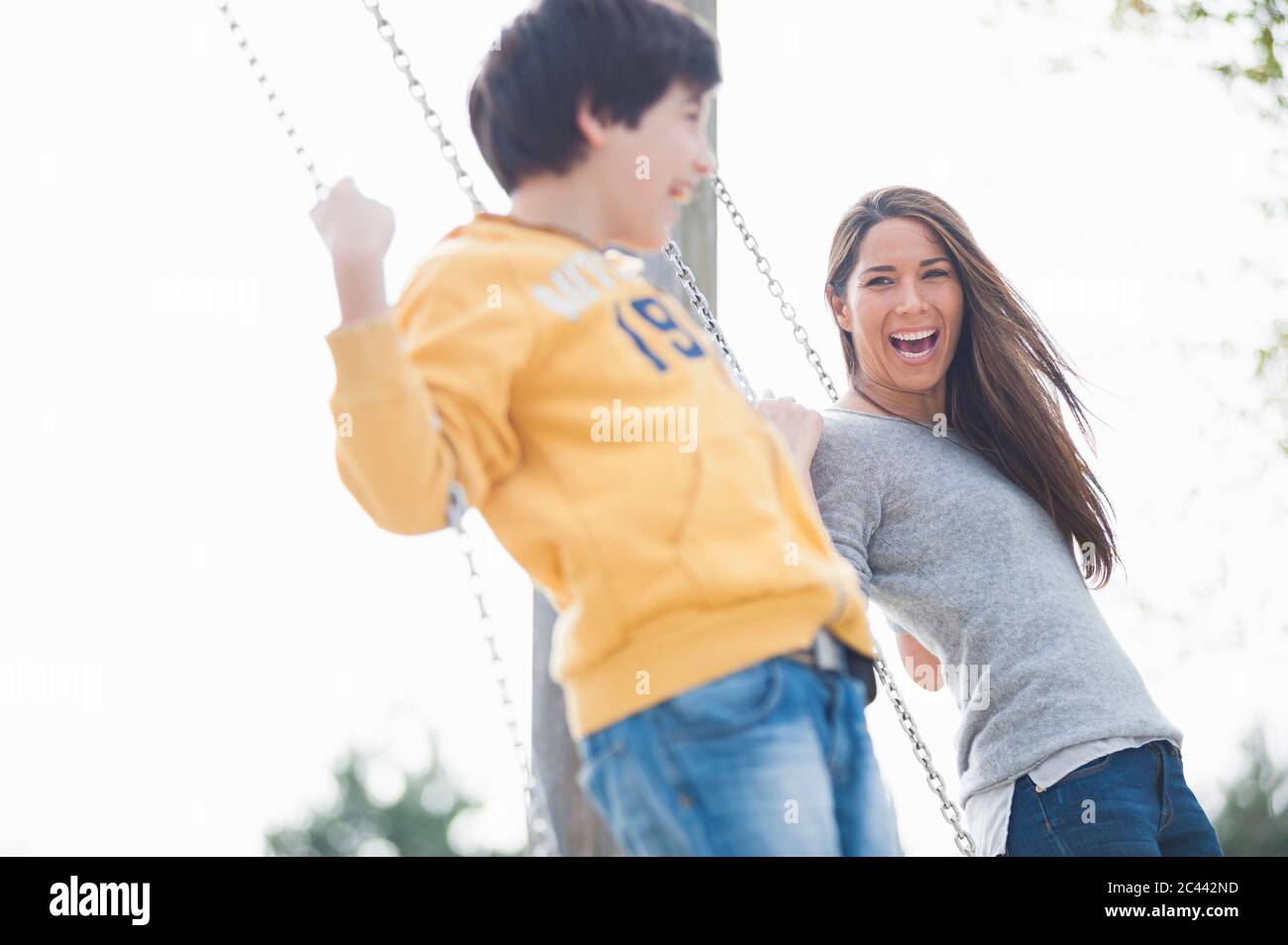 Fröhliche Mutter und Sohn schwingen im Park gegen klaren Himmel Stockfoto
