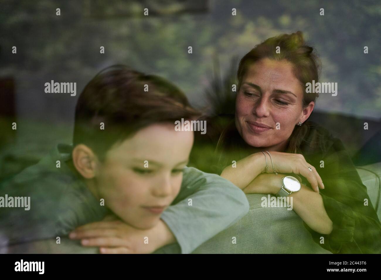 Nachdenkliche Mutter mit Sohn, die sich zu Hause auf dem Sofa entspannt, durch das Fenster gesehen Stockfoto