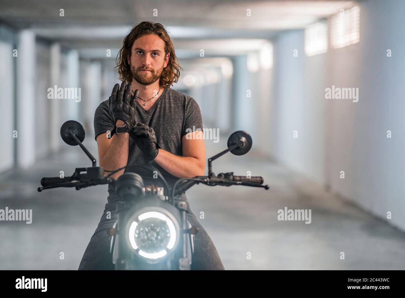 Junger Mann, der seine Handschuhe auf dem Motorrad aufsetzt Stockfoto