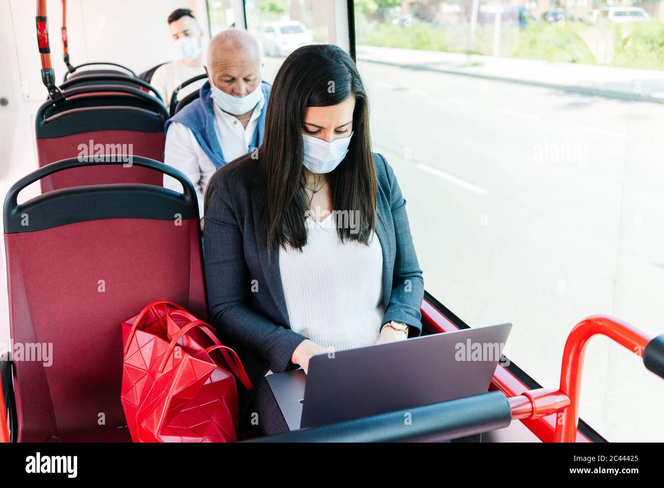 Frau trägt Schutzmaske in öffentlichen Bus mit Laptop, Spanien Stockfoto