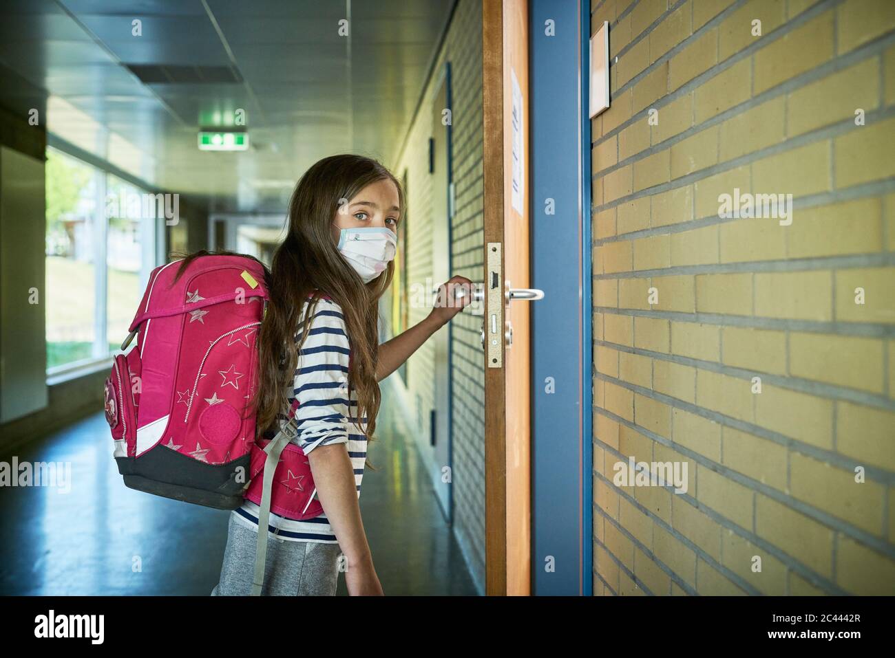 Mädchen trägt Maske in der Schule öffnen Klassentür Stockfoto