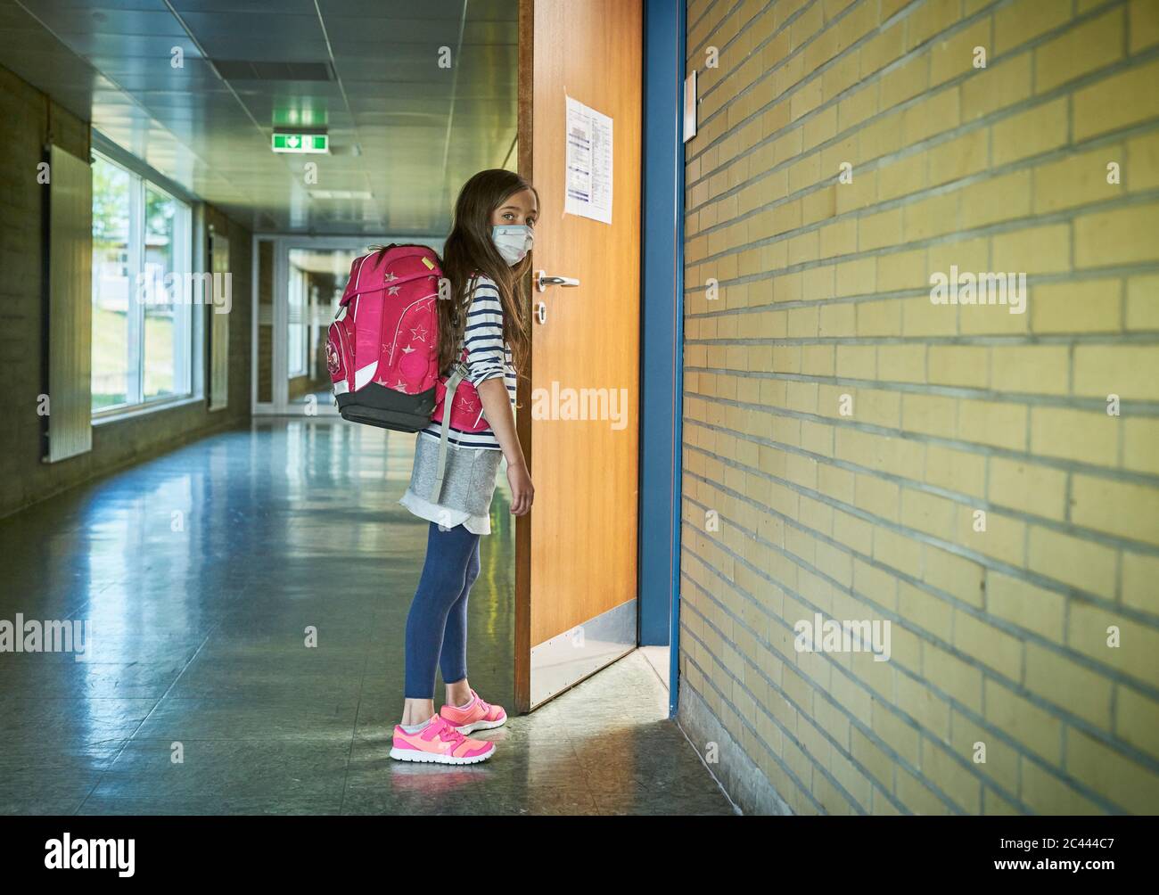 Mädchen trägt Maske in der Schule öffnen Klassentür Stockfoto