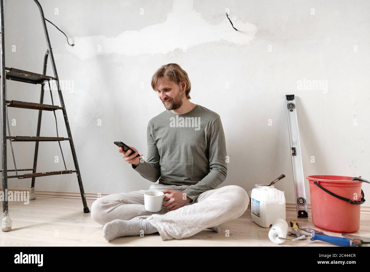 Glücklicher Mann mit Smartphone während der Pause von der Malerei zu Hause Stockfoto