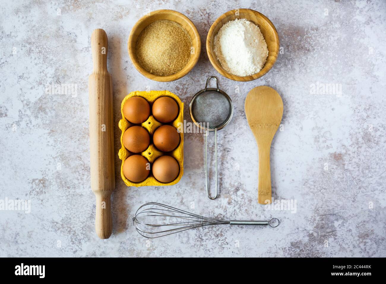 Nudelholz, Drahtquirl, Sieb, Hühnereier, Löffel und Schüsseln mit Mehl und braunem Zucker Stockfoto