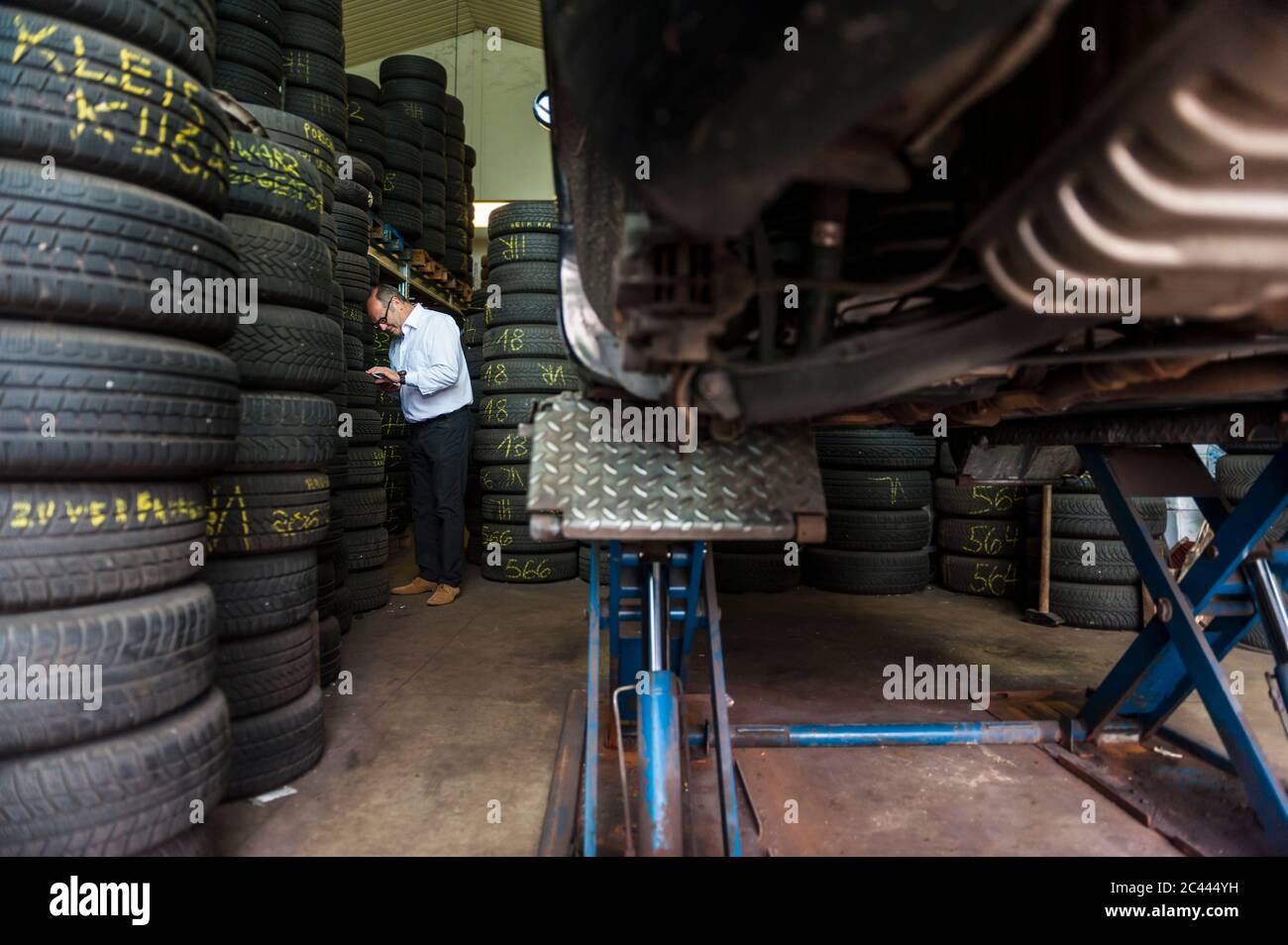 Leitender männlicher Unternehmer, der bei Reifenstapeln im Geschäft steht Stockfoto