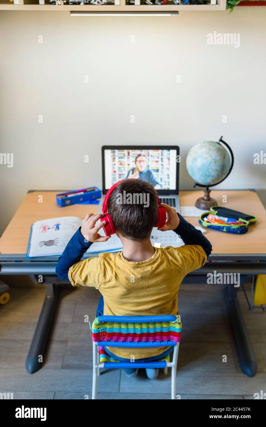 Rückansicht des Schülers, der während der Heimsschooling dem Lehrer über Kopfhörer zuhört Stockfoto