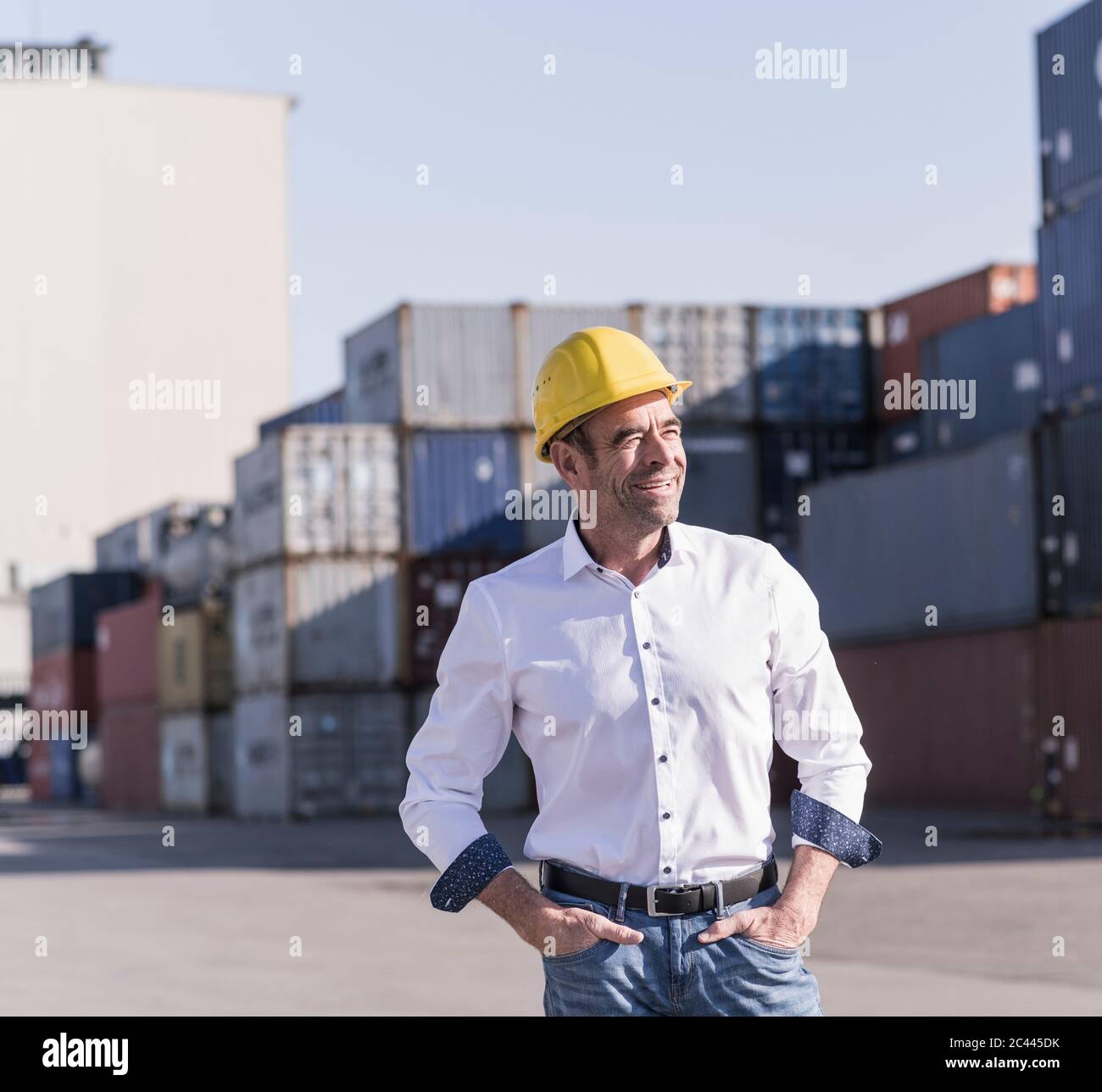 Porträt eines entspannten Geschäftsmannes mit Schutzhelm vor Frachtcontainern Stockfoto