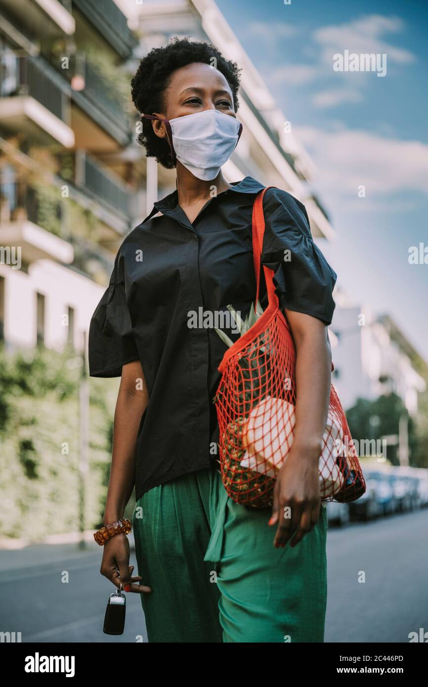 Porträt einer jungen Frau mit Schutzmaske auf der Straße mit ihrem Kauf stehen Stockfoto