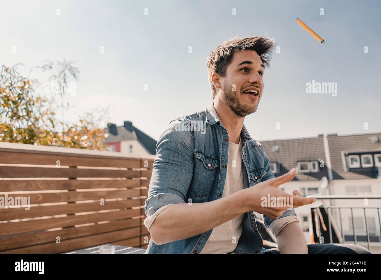 Lachender junger Mann, der Bleistift in die Luft splättert Stockfoto