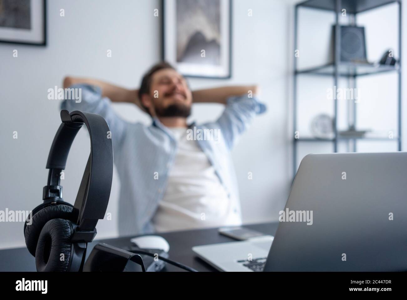 Mann lehnt sich zurück am Schreibtisch, konzentrieren sich auf Kopfhörer Stockfoto