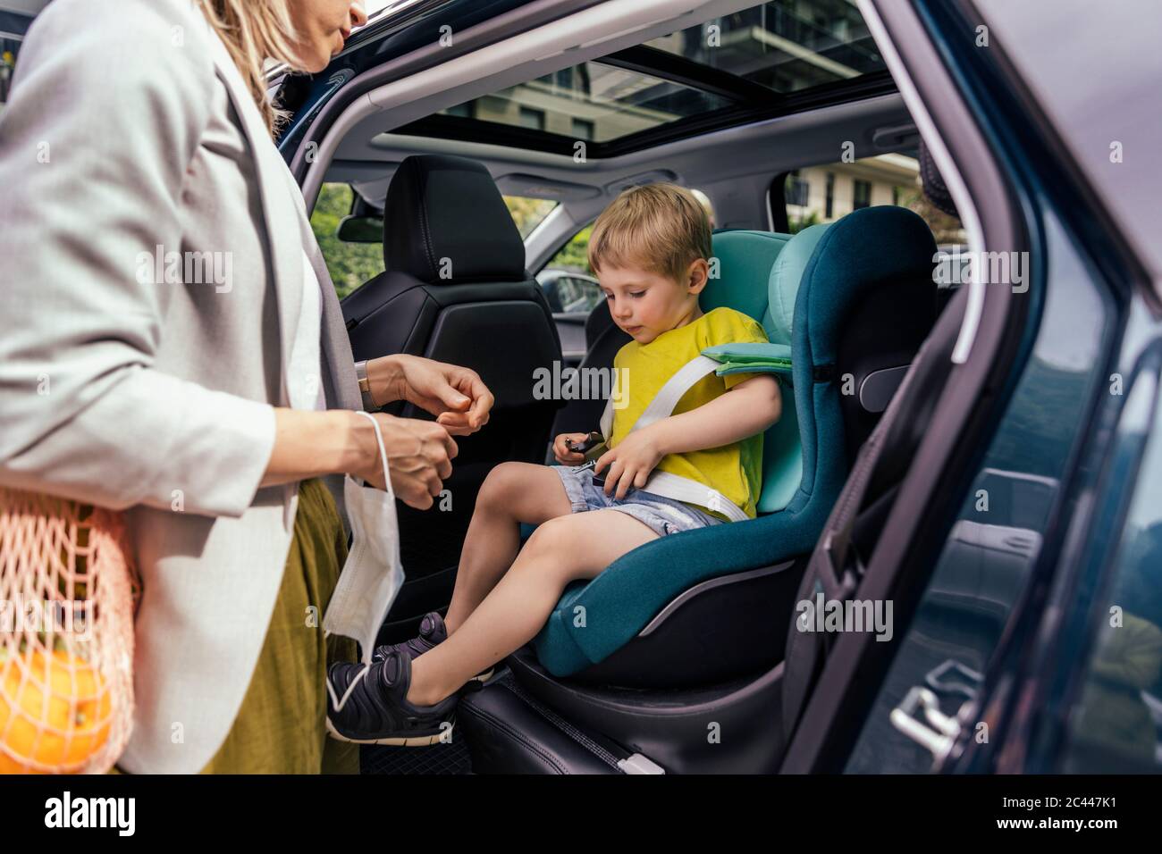 Kleiner Junge Befestigung Sitzglocke Kindersitz im Auto, während seine Mutter ihn beobachtet Stockfoto