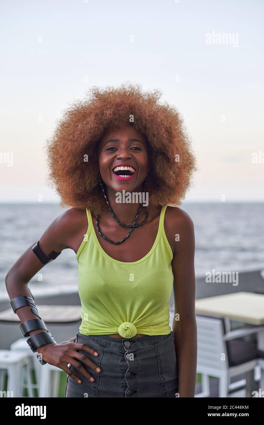 Porträt einer lachenden Frau mit afro Frisur, die vor dem Meer steht Stockfoto