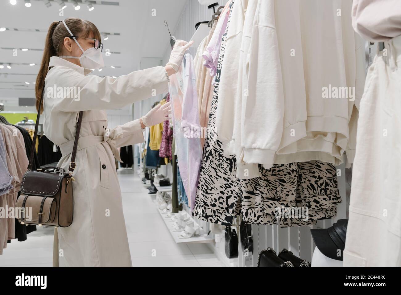 Frau mit Gesichtsmaske und Einweghandschuhe Einkaufen in einem Modehaus Stockfoto