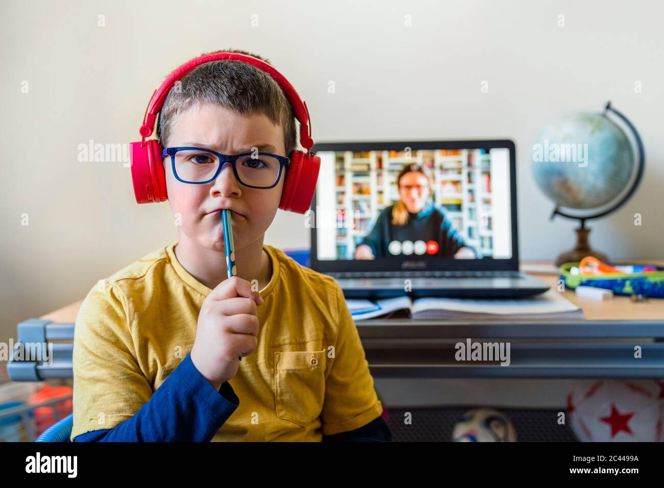 Nachdenklicher Junge sitzt während eines Videoanrufs zu Hause gegen den Laptop Stockfoto