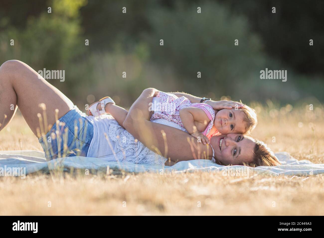 Portrait einer lächelnden Frau und Tochter, die während eines sonnigen Tages auf einer Picknickdecke auf der Wiese liegen Stockfoto