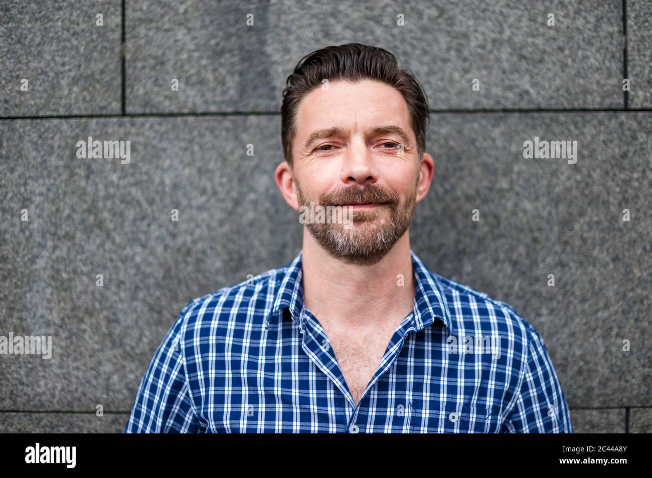 Porträt eines selbstbewussten, gutaussehenden Mannes, der in der Stadt gegen eine graue Mauer steht Stockfoto