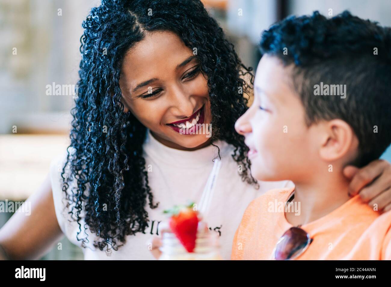 Lächelnde Frau, die den Jungen beim Smoothie-Trinken im Restaurant ansieht Stockfoto