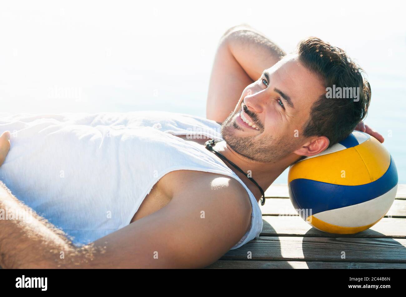 Porträt eines lächelnden jungen Mannes mit Ball auf dem Steg vor einem See Stockfoto