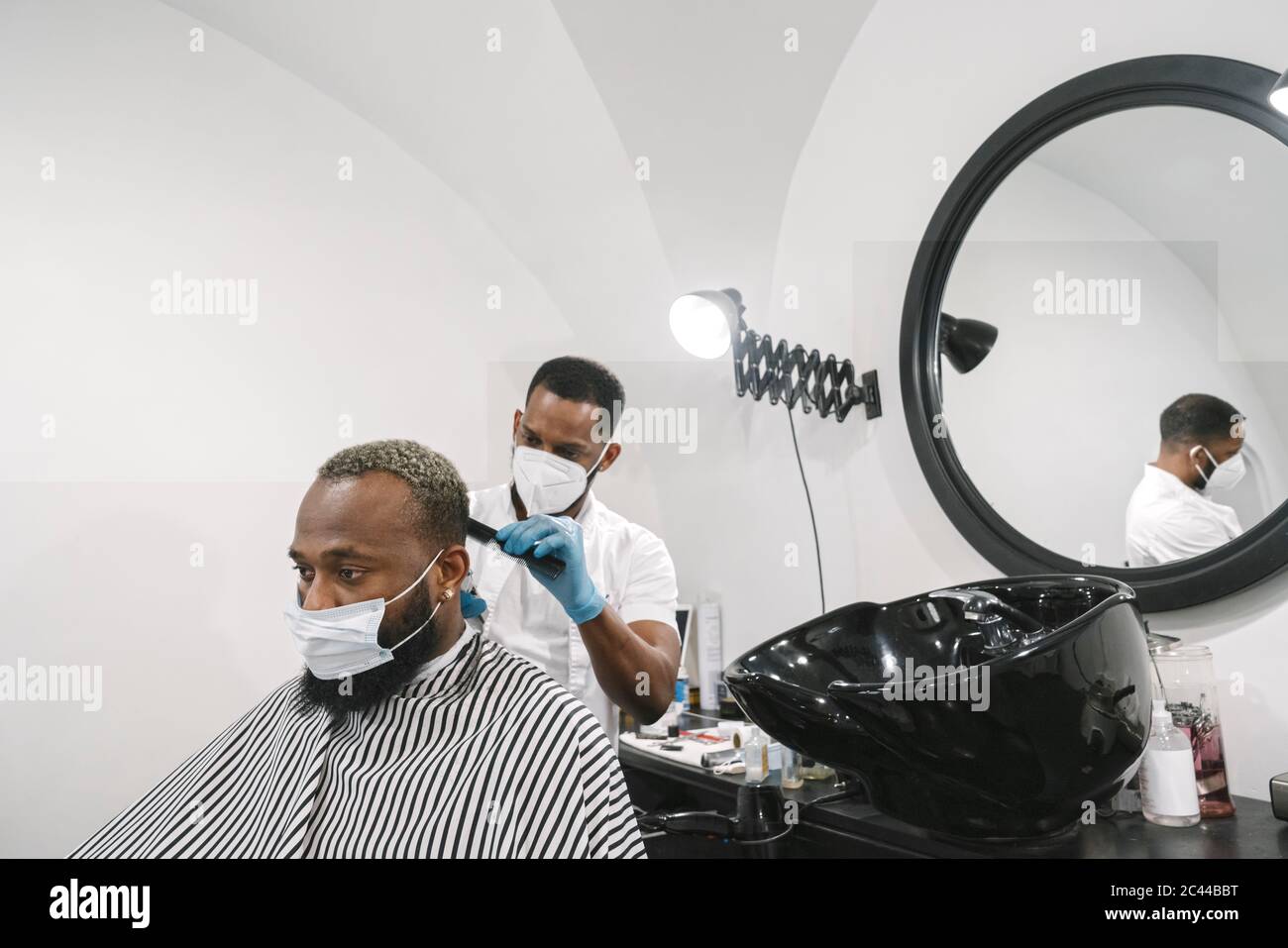 Friseur trägt chirurgische Maske und Handschuhe tun Haar des Kunden Stockfoto