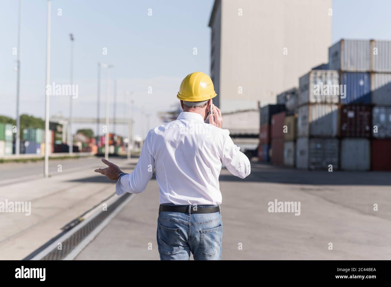 Rückansicht des Geschäftsmannes am Telefon, der Schutzhelm auf dem Industriegelände trägt Stockfoto