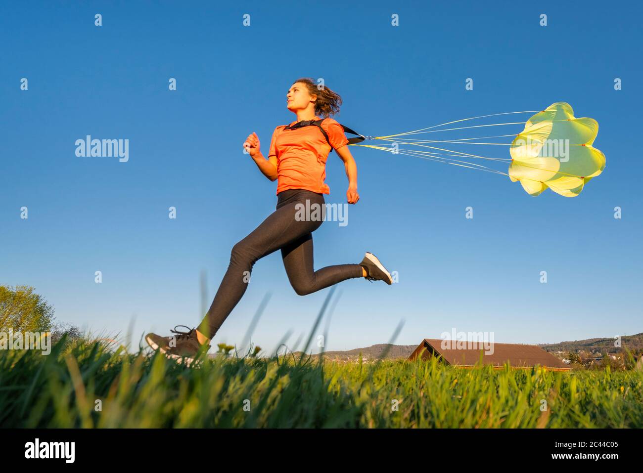 Low-Angle-Ansicht der jungen Frau sprintet mit Fallschirm gegen klaren blauen Himmel Stockfoto