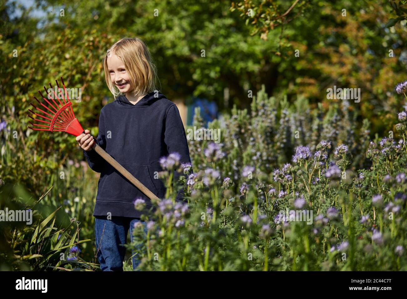 Lächelndes Mädchen im Garten mit einem Rechen Stockfoto