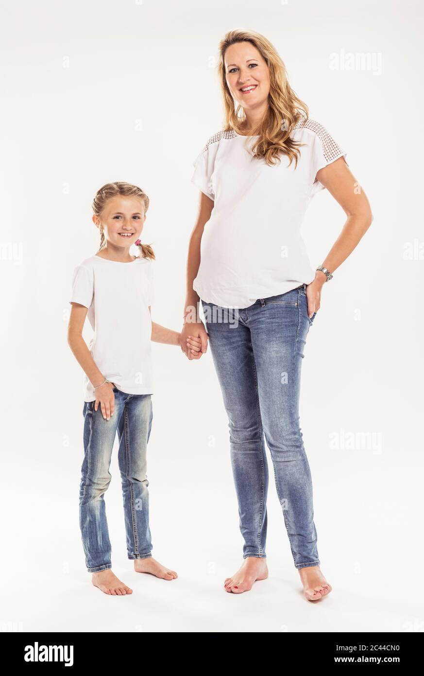 Portrait einer glücklichen schwangeren Frau, die Hand in Hand mit ihrer Tochter vor weißem Hintergrund steht Stockfoto