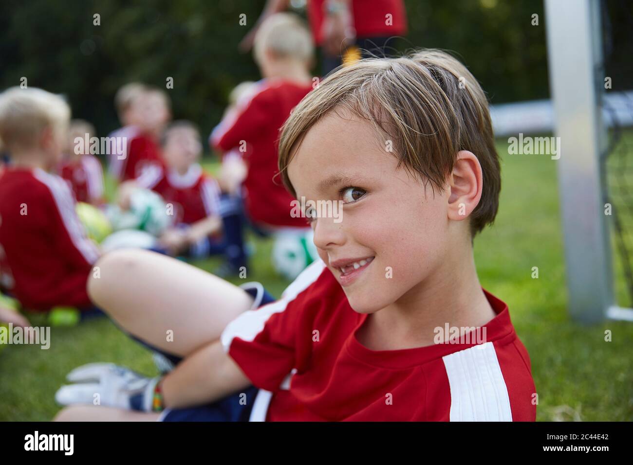 Porträt des verspielten Jungen mit Fußballmannschaft im Hintergrund auf dem Feld Stockfoto