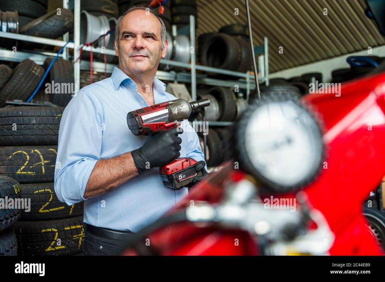 Selbstbewusster Geschäftsmann mit Schlagschrauber beim Blick auf den Reifenladen Stockfoto