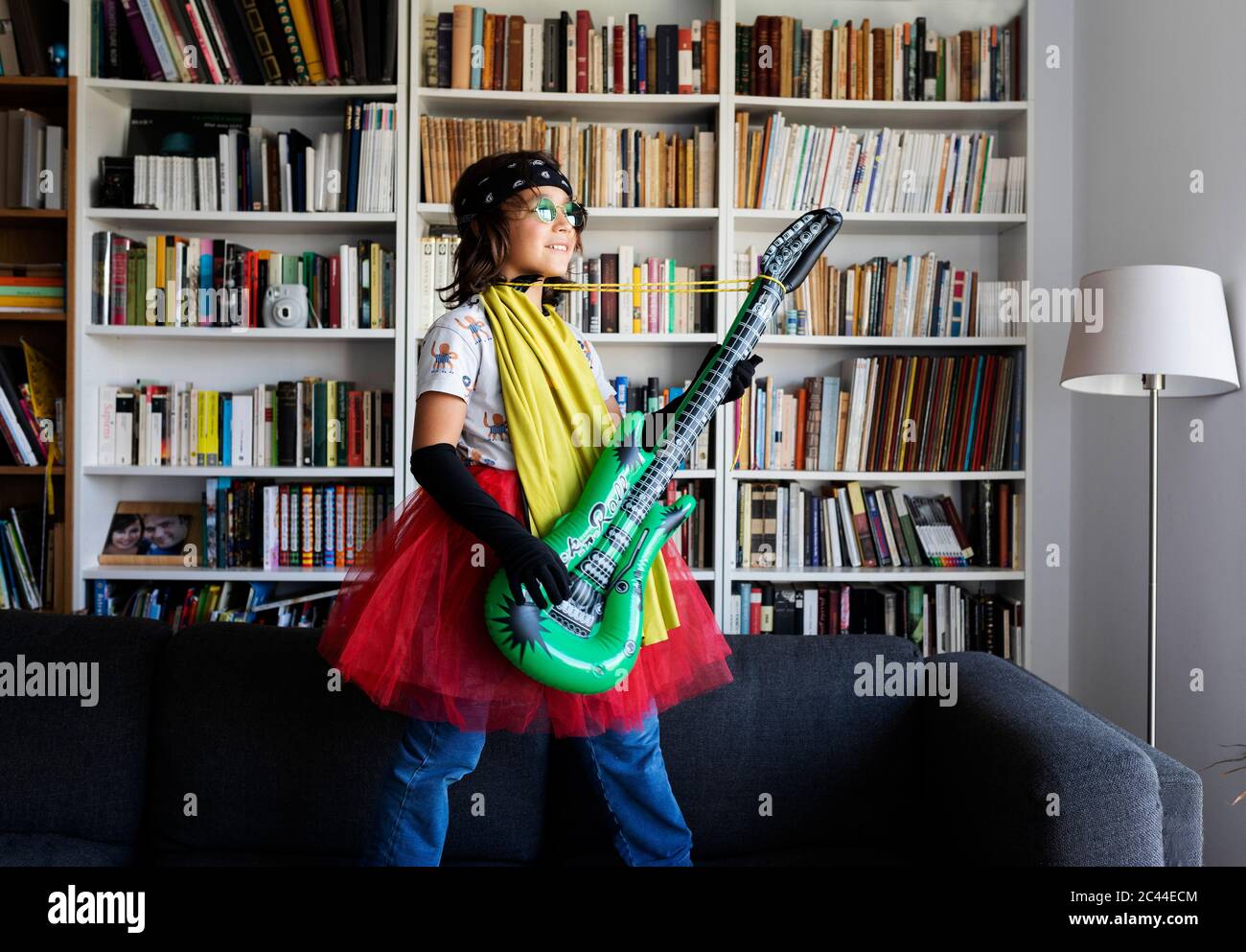 Happy Boy verkleidet als Rockstar stehen auf der Couch zu Hause mit aufblasbaren Spielzeuggitarre Stockfoto
