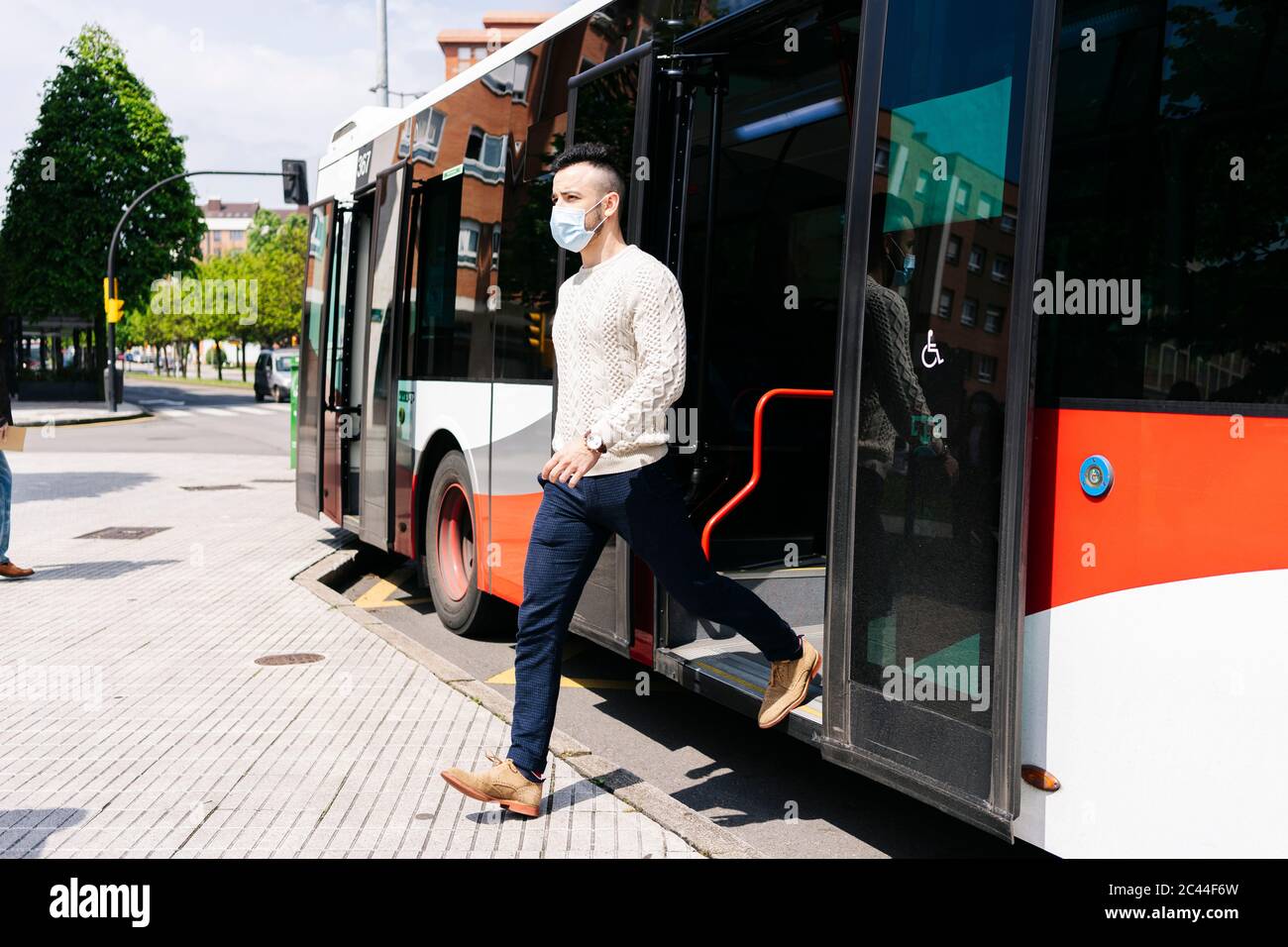 Junger Mann mit Schutzmaske beim Aussteigen aus dem öffentlichen Bus, Spanien Stockfoto