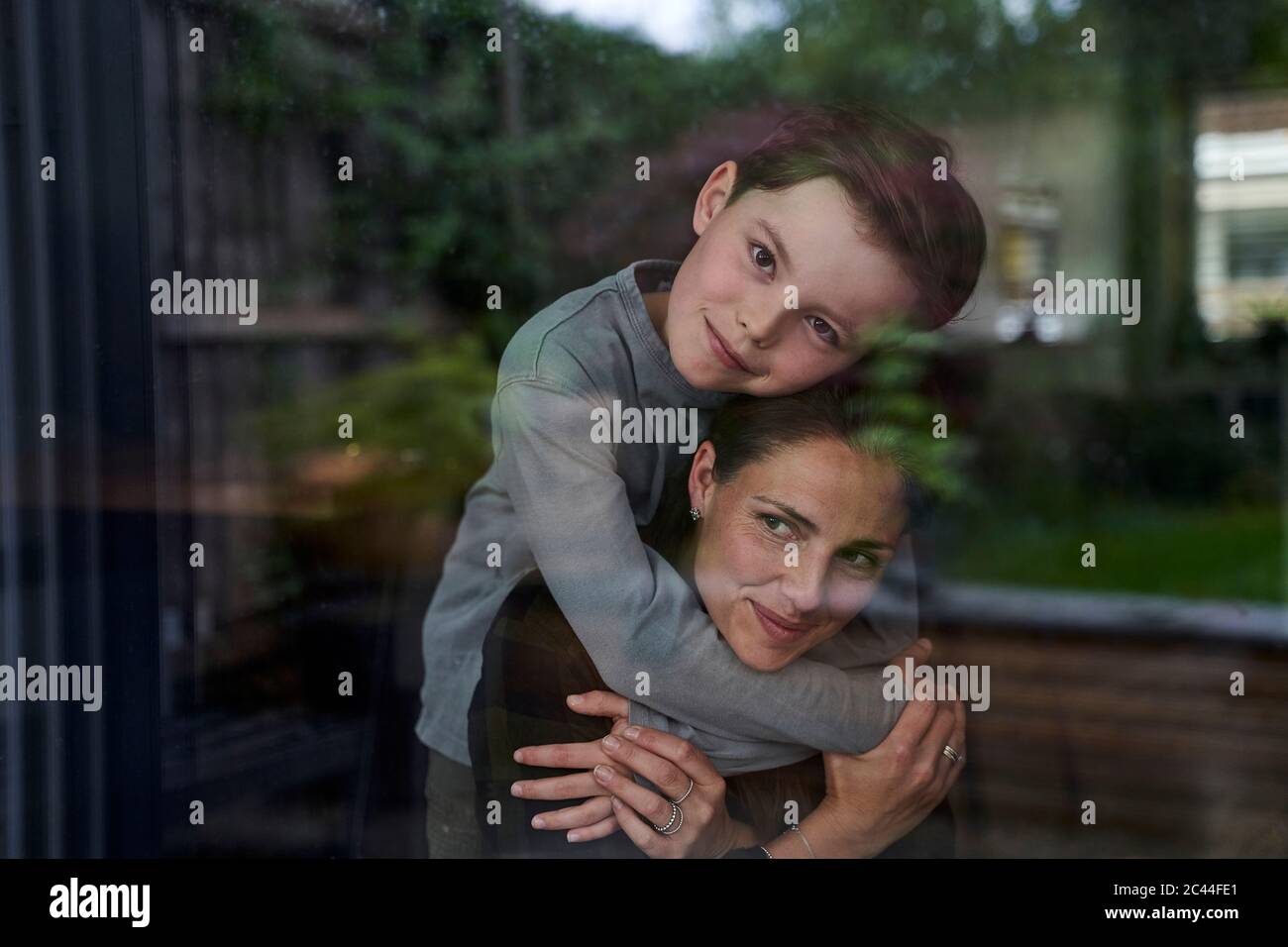 Liebevoller Sohn umarmt Mutter, während zu Hause durch Fenster gesehen Stockfoto