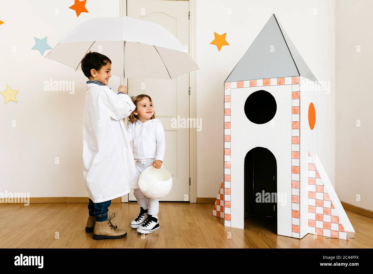 Geschwister spielen Astronaut und Forscher mit Regenschirm bei Rakete Stockfoto