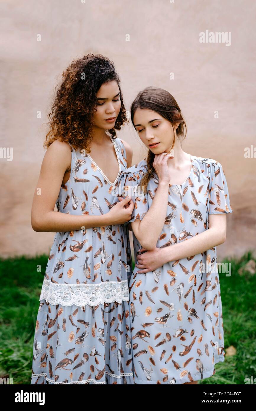 Liebevolle Schwestern tragen Kleider mit geschlossenen Augen stehen gegen alte Wand Stockfoto