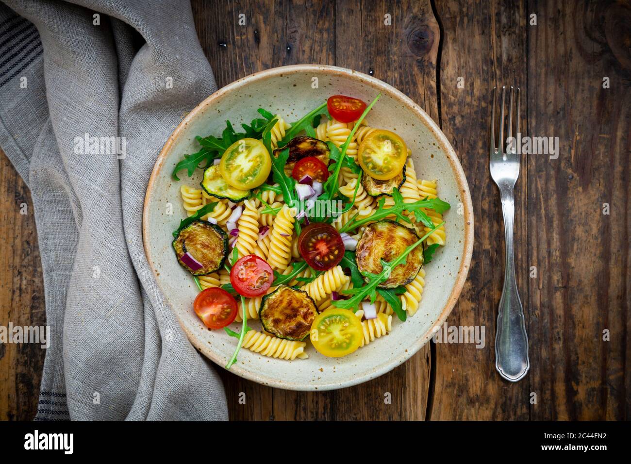 Schüssel Nudelsalat mit gegrillten Zucchini, Tomaten, Rucola, spanische Zwiebel und Balsamico-Essig Stockfoto