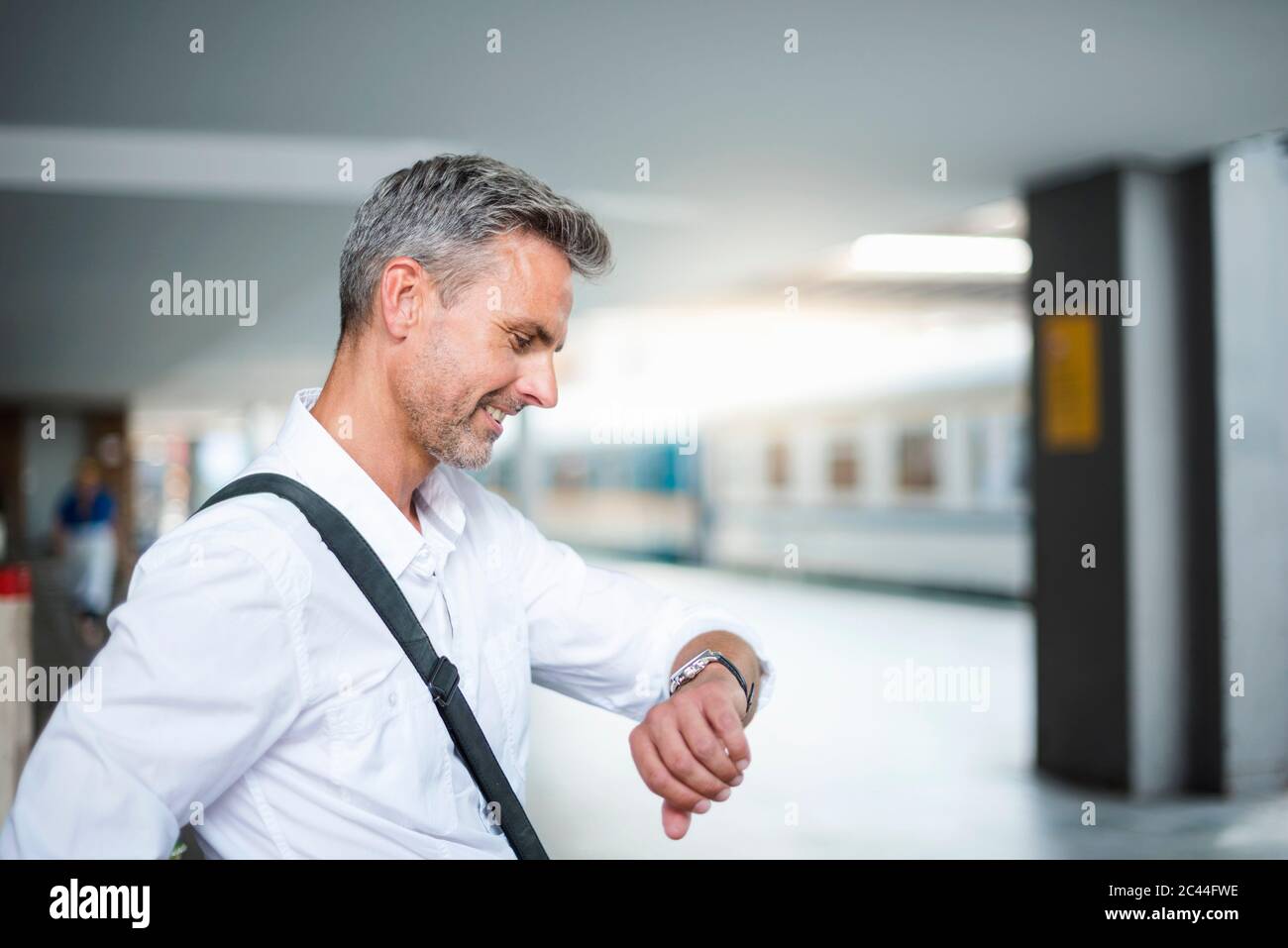 Geschäftsmann, der Zeit überprüft, während er am Bahnhofssteig sitzt Stockfoto