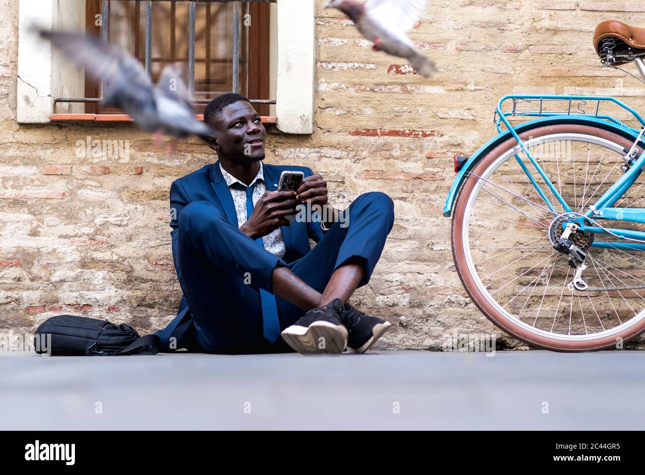 Junger Geschäftsmann mit Smartphone auf dem Boden in der Stadt sitzen Stockfoto