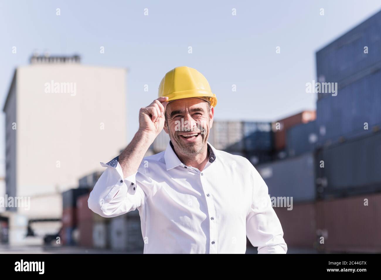 Portrait eines lachenden Geschäftsmannes mit Schutzhelm auf dem Industriegelände Stockfoto