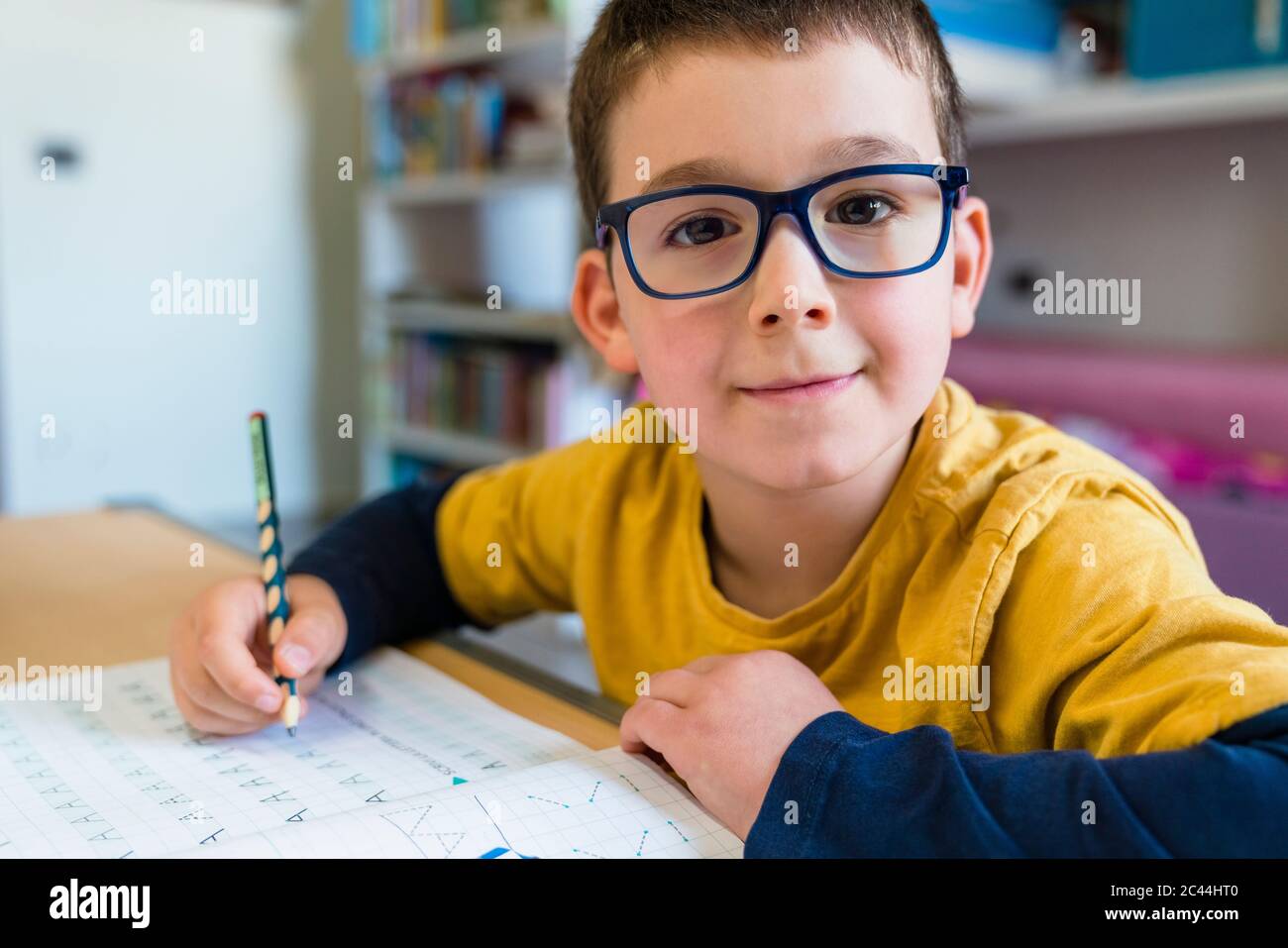 Netter Junge, der Hausaufgaben macht, während er während des Coronavirus am Schreibtisch sitzt Stockfoto