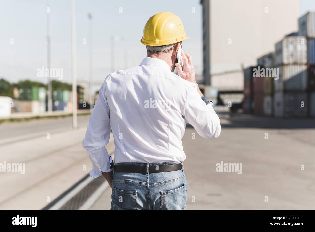 Rückansicht des Geschäftsmannes am Telefon, der Schutzhelm auf dem Industriegelände trägt Stockfoto
