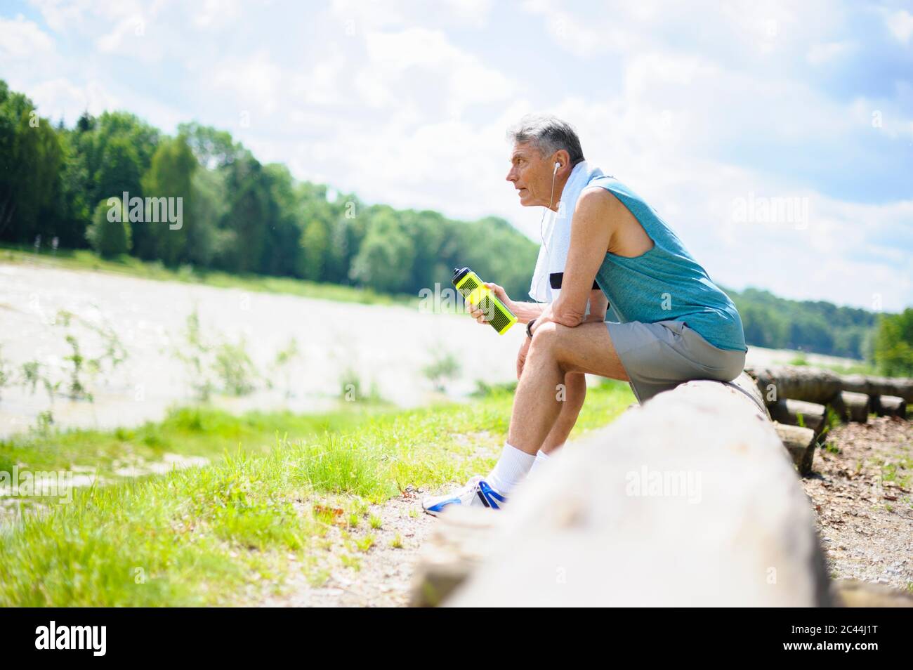 Volle Seitenansicht des erschöpften älteren Mannes im Ruhestand, der auf dem Holzbuch sitzt, während er an sonnigen Tagen auf das Flussufer blickt Stockfoto
