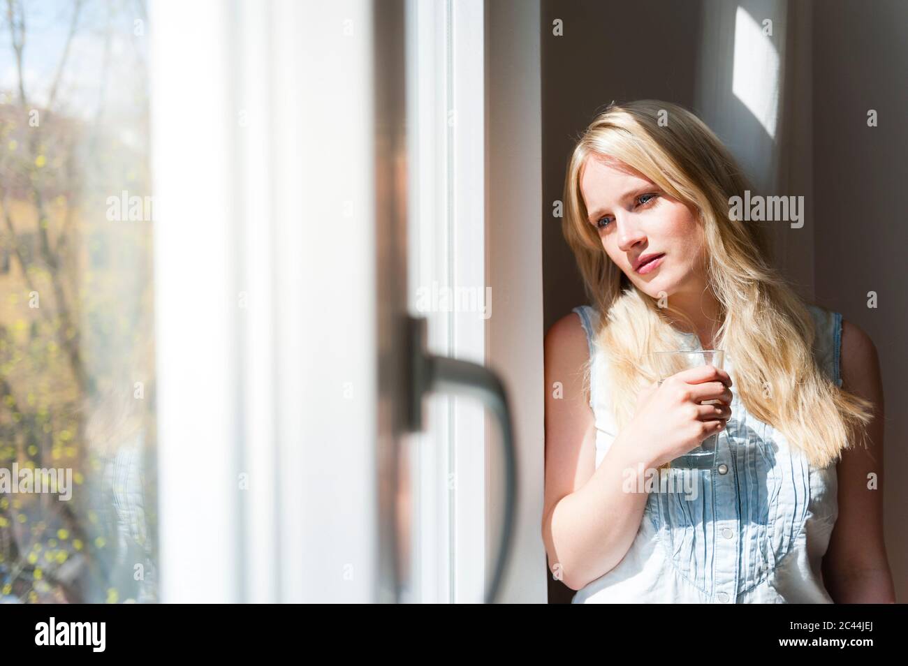 Porträt einer ernsthaften blonden Frau, die aus dem Fenster schaut Stockfoto