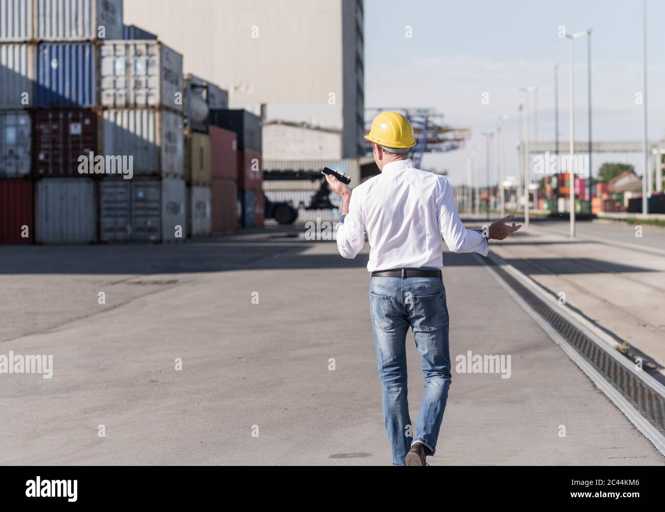 Rückansicht des Geschäftsmannes, der Schutzhelm mit Handy auf Industriegelände trägt Stockfoto