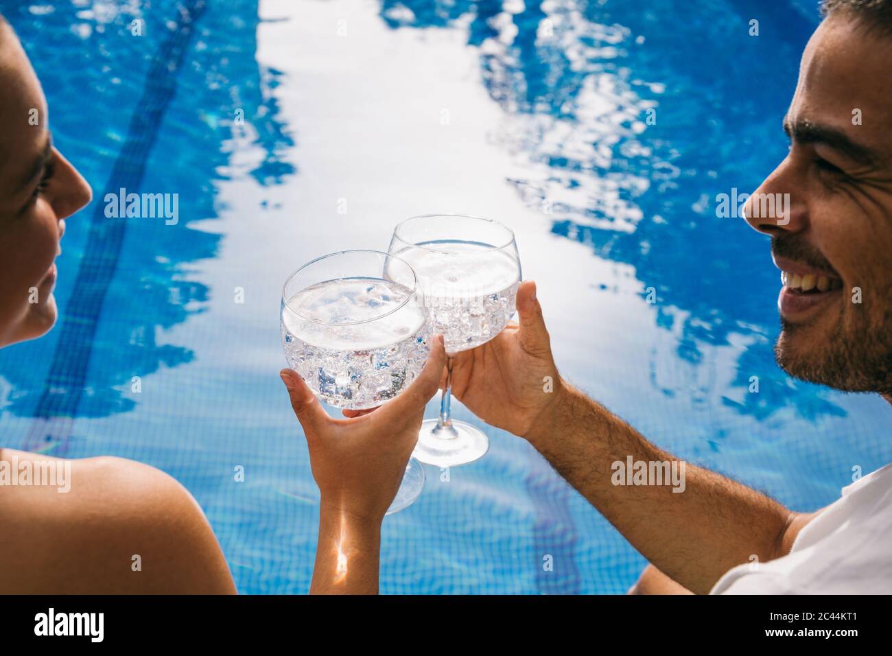 Fröhliches junges Paar, das sich anschaut, während es Getränke am Pool toast Stockfoto
