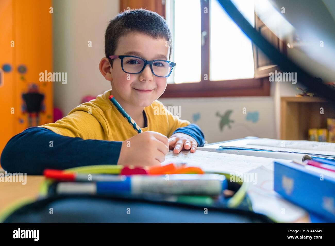 Lächelnder männlicher Student, der während des Coronavirus mit Büchern am Schreibtisch sitzt Stockfoto