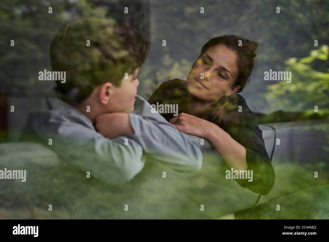 Mutter und Sohn reden während sie sich auf dem Sofa zu Hause entspannen, durch das Fenster gesehen Stockfoto