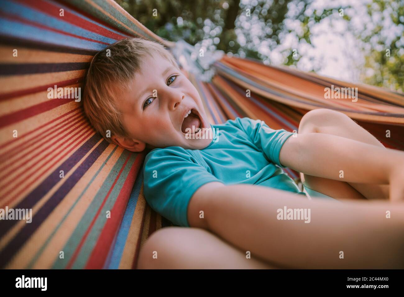 Verspielter Junge liegt auf Hängematte mit offenem Mund im Garten Stockfoto
