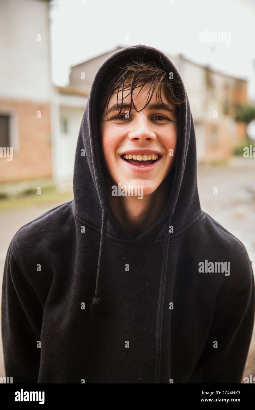 Fröhlicher Teenager Junge trägt schwarze Kapuzen-Sweatshirt im Freien Stockfoto